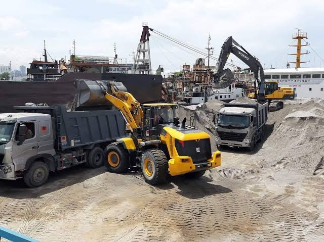 Dump trucks and loader moving sand at a worksite